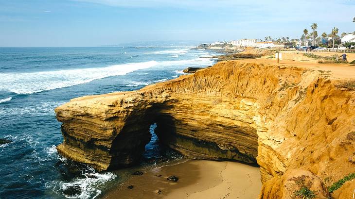 A cliff next to the ocean with palm trees and buildings in the distance A cliff next to the ocean with palm trees and buildings in the distance