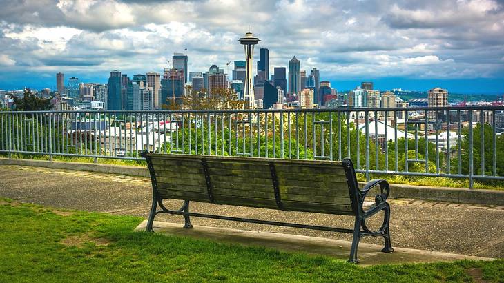 A bench on the grass with a path and a view of a city skyline in front of it A bench on the grass with a path and a view of a city skyline in front of it