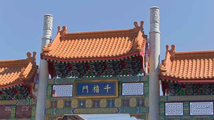 The orange roofs of a pagoda-like gate in a Chinatown against blue sky