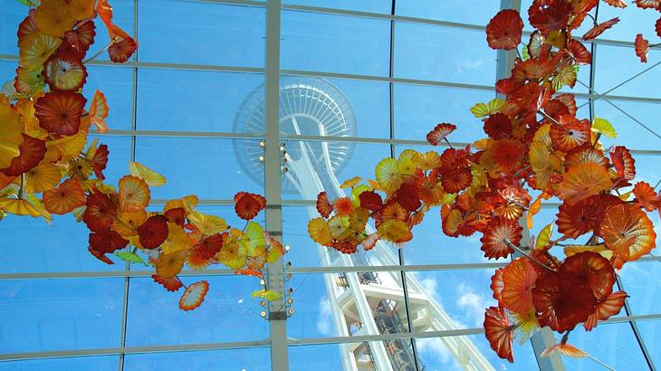 Red, orange, and yellow glass flowers in front of a window and an observation tower Red, orange, and yellow glass flowers in front of a window and an observation tower
