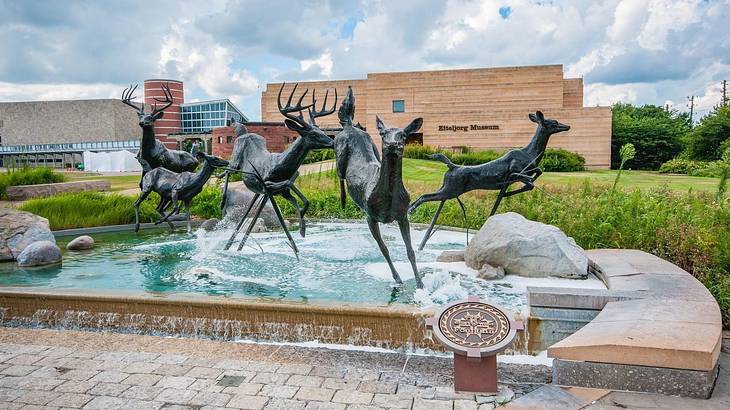 A statue of five deer over a fountain with a museum building behind it
