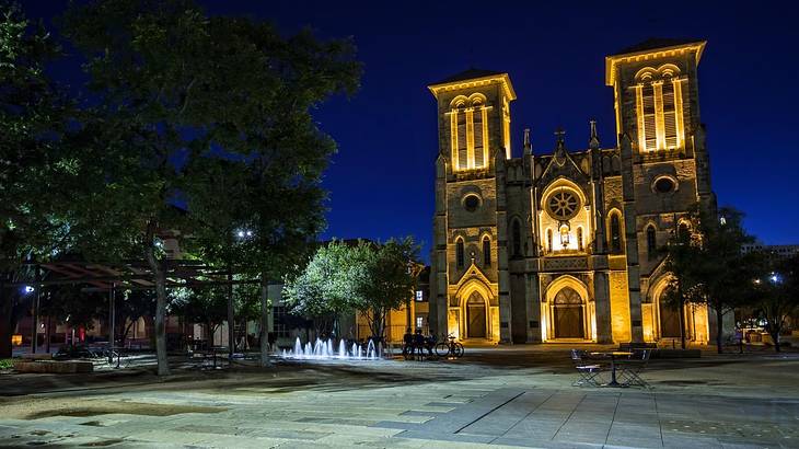 A church with two towers sitting in a square and illuminated at night