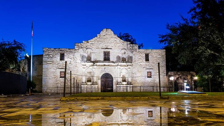 An old stone structure lit up with a wet path in front of it at night