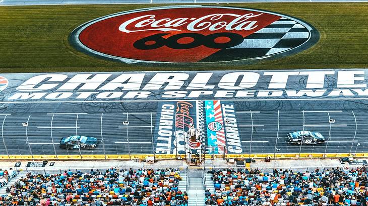 A racecar track with cars, an audience of fans, and a coca cola logo on the grass