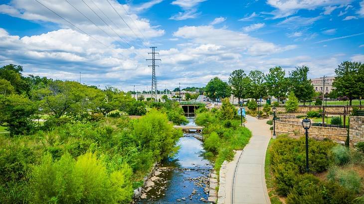 A creek with a path next to it and greenery surrounding it A creek with a path next to it and greenery surrounding it