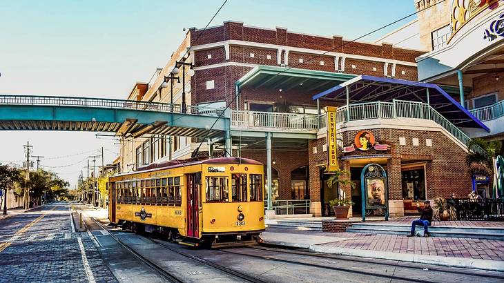 A yellow street car on the road with red brick buildings to the side