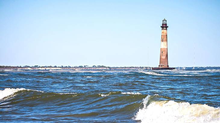 Ocean water with waves and a red and white striped lighthouse in the distance