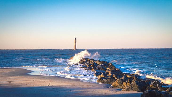 Ocean waves crashing onto a beach with a lighthouse in the distance