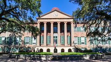 A building with columns and trees and grass in front of it