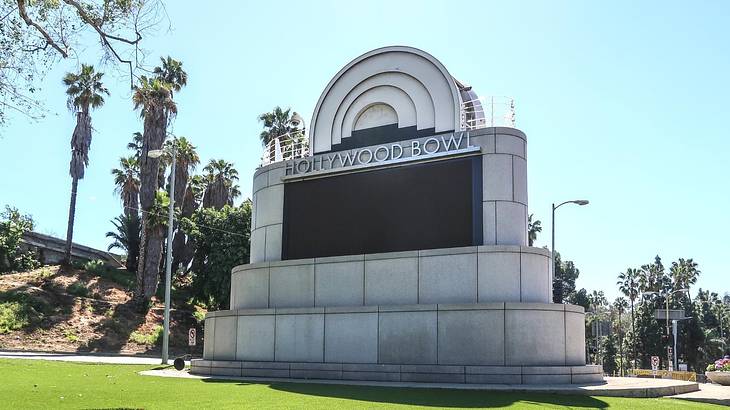 A sign that says "Hollywood Bowl" with grass and palm trees around it