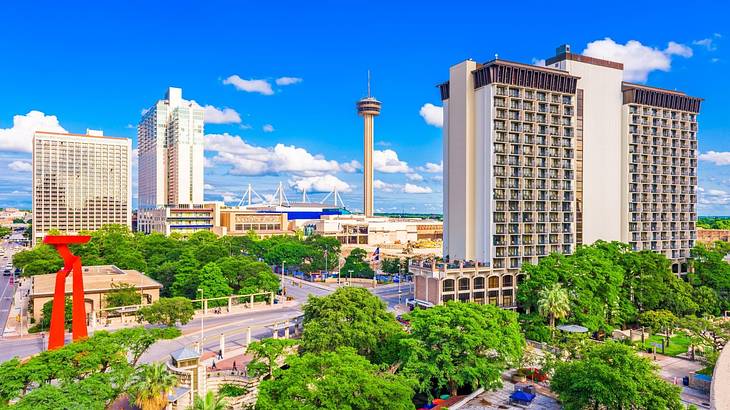 A city skyline with tall buildings, an observation tower, and trees under a blue sky A city skyline with tall buildings, an observation tower, and trees under a blue sky
