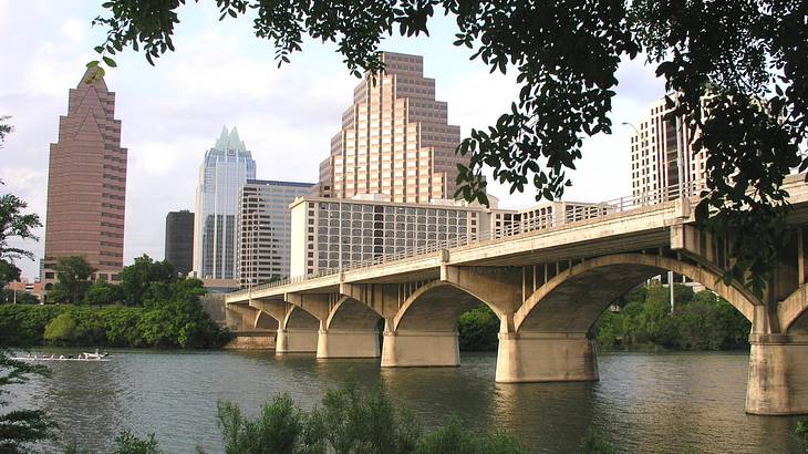 A bridge over water with trees in the foreground and buildings in the background