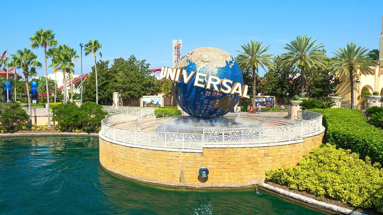 A globe sculpture that says "Universal" on it next to a pond and palm trees