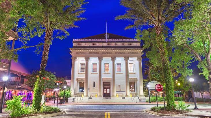 A stone building with columns with a palm tree-lined street in front of it