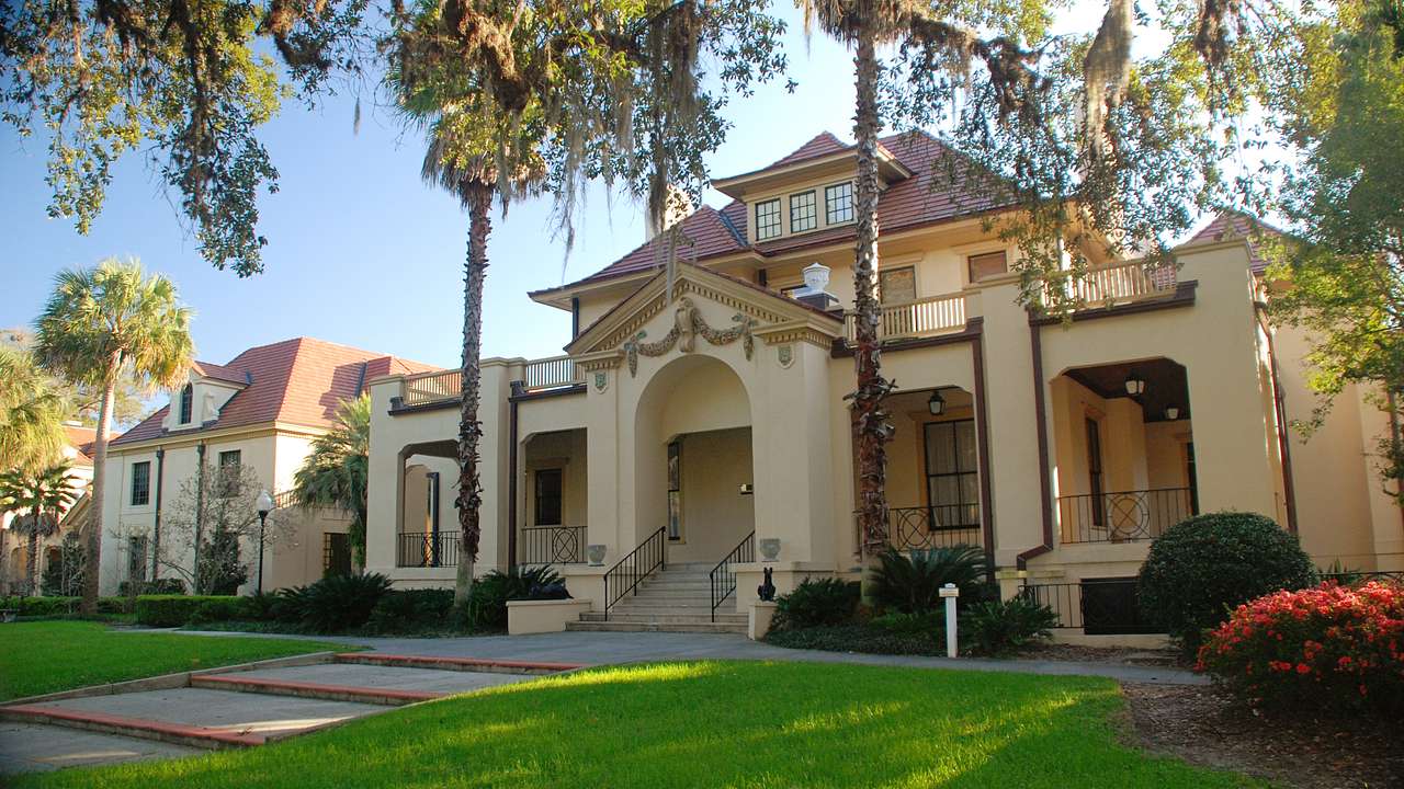 A Mediterranean Revival-style building with grass and palm trees in front of it