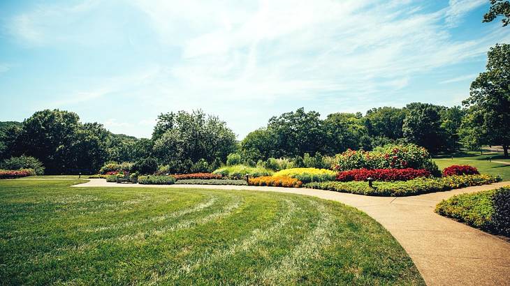Green grass with a path through it and colorful flower gardens and trees to the side