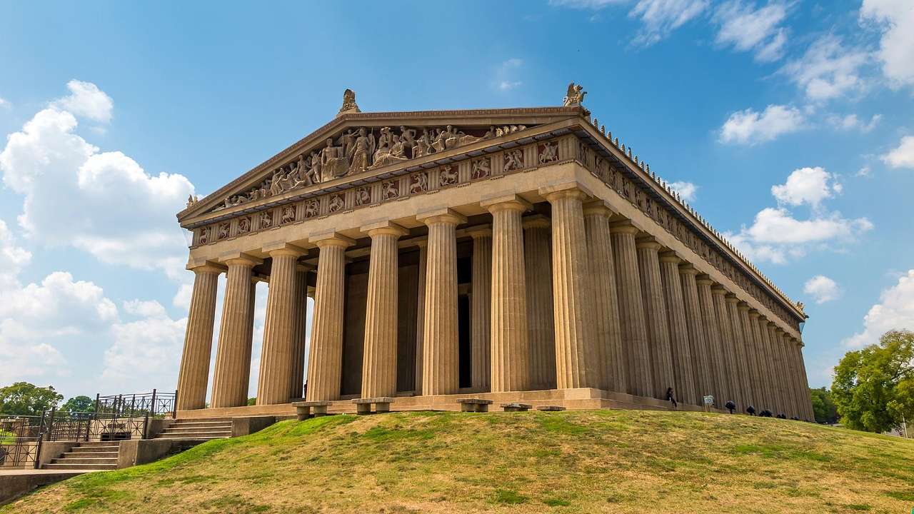 A replica of the Greek Parthenon surrounded by grass on a clear day