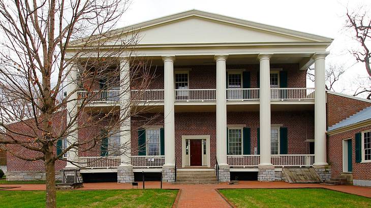 A mansion-style red brick house with white columns and a lawn and path in front of it