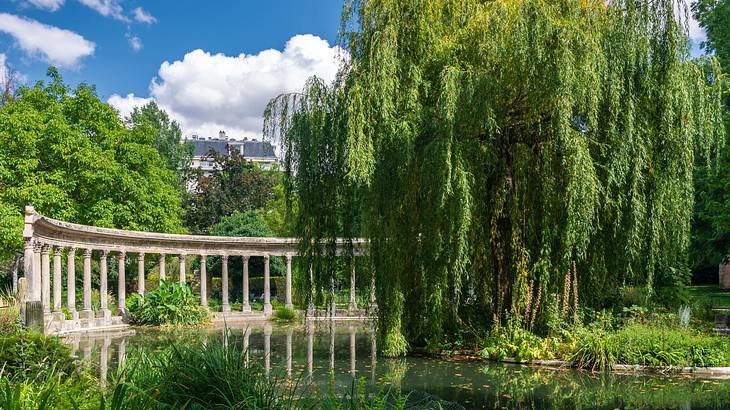 A stone column structure on the side of a pond with greenery surrounding them