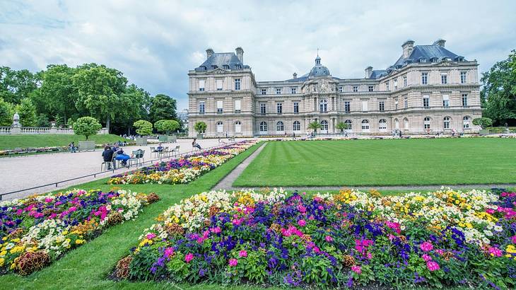 A lawn with colorful flower beds and a mansion-style building in the background