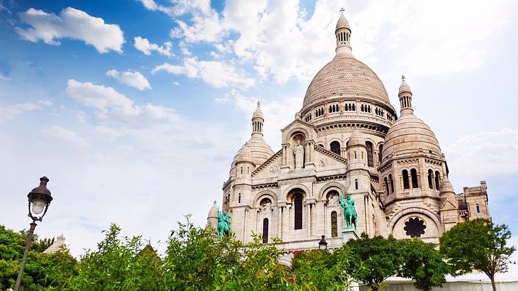 A cathedral with three domed roofs and trees and a lamppost in front of it