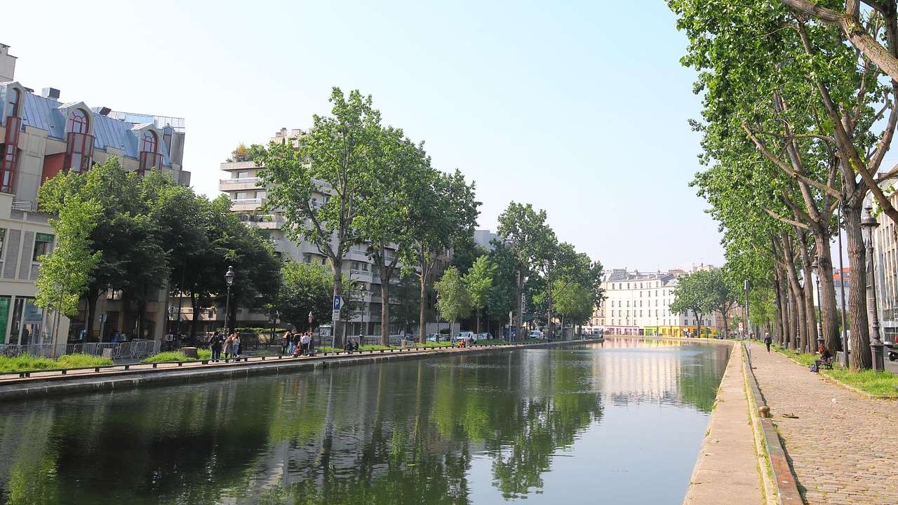A canal with a path and trees on one side and buildings on the other side