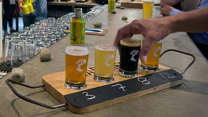 A person picking up a beer from a flight of four beers on a bar