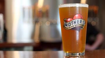 A pint of beer on a bar in a glass that says "Mother's Brewing Company"
