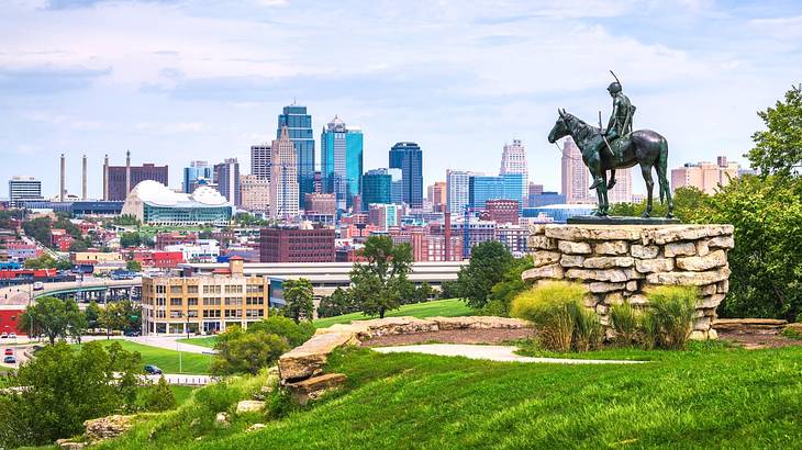 A view of a skyline from a park with greenery and a statue