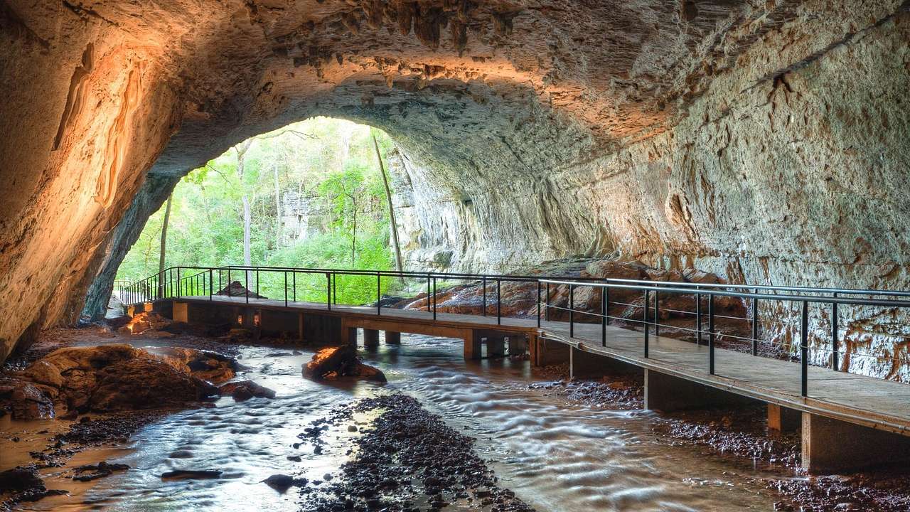 A cave with a walkway through it and a view of trees outdoors