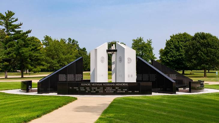 A white and black memorial structure with path, grass, and trees around it