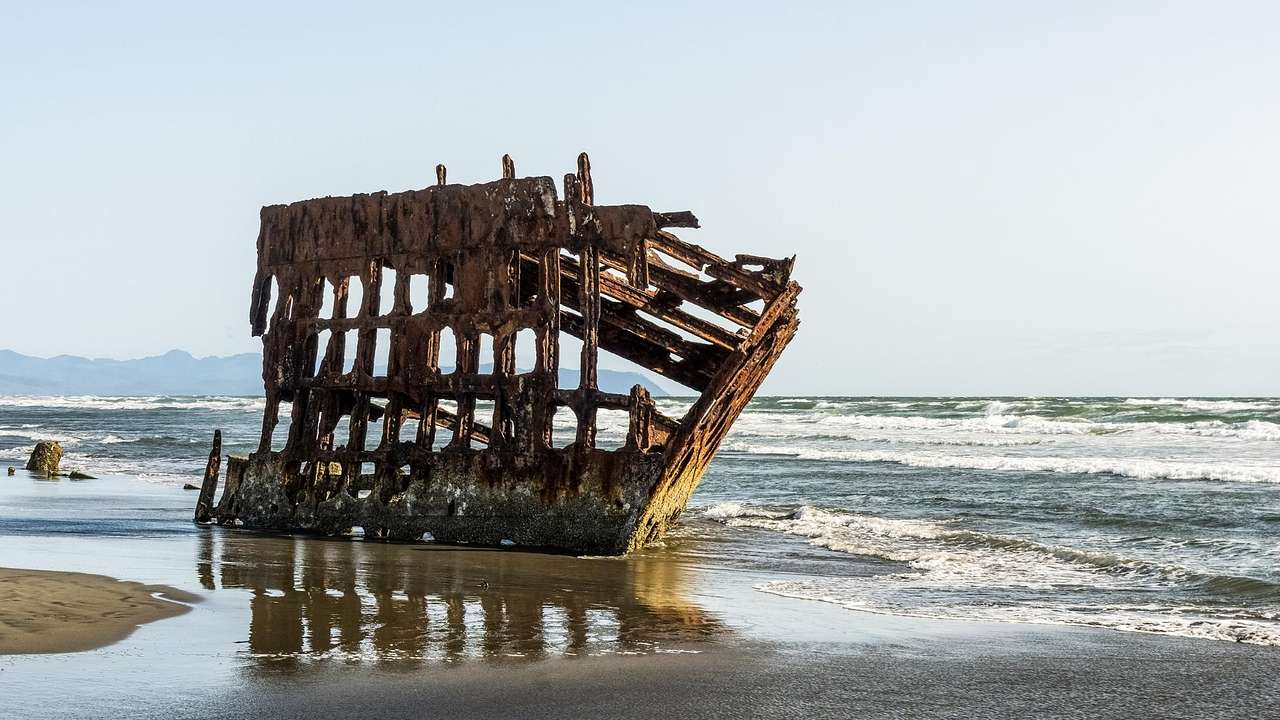 A shipwreck on the sand with ocean water surrounding it