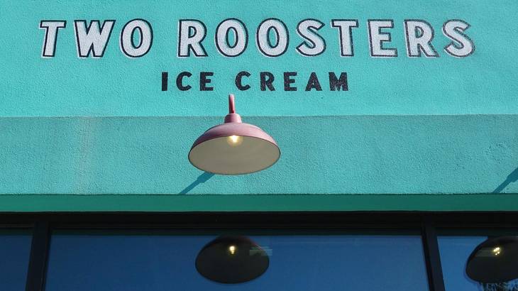 A turquoise wall with a "Two Roosters Ice Cream" sign and a lamp underneath it