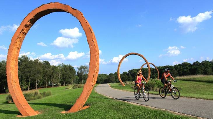 A path through the grass with ring sculptures on it and people biking