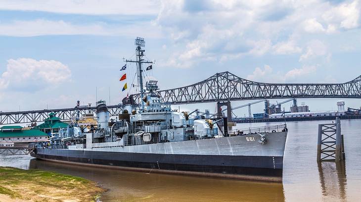 A navy ship on the water with a bridge behind it