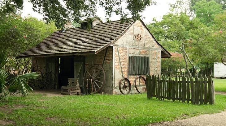 An old fashioned brick barn with a fence, grass, and trees around it