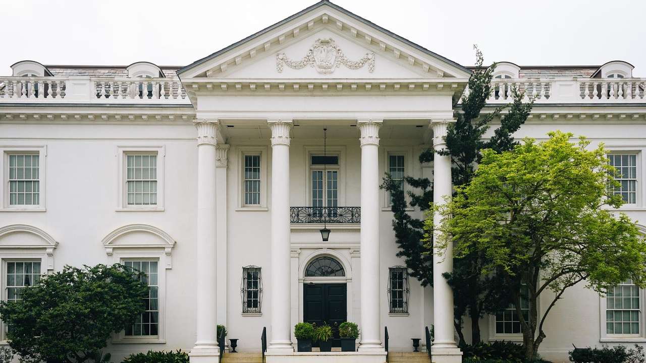 A white mansion with a black door and trees in front of it