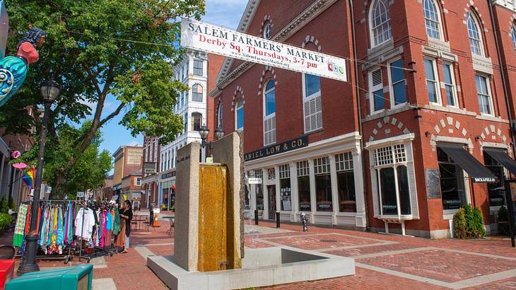 A street with a red brick building, a farmers market banner, and a clothing stall