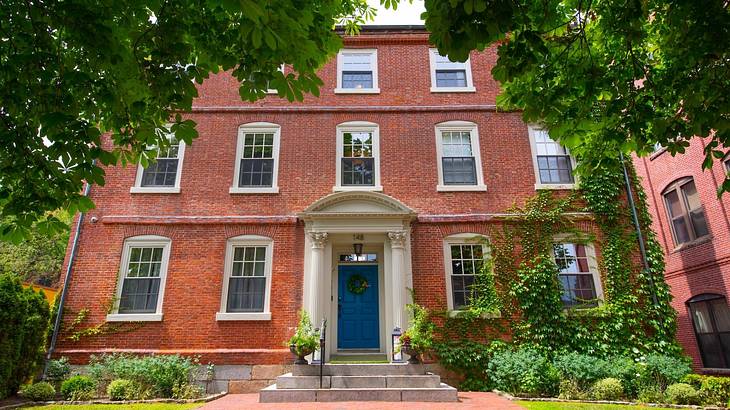 A mansion-style house with white windows, a blue front door, and greenery surrounding