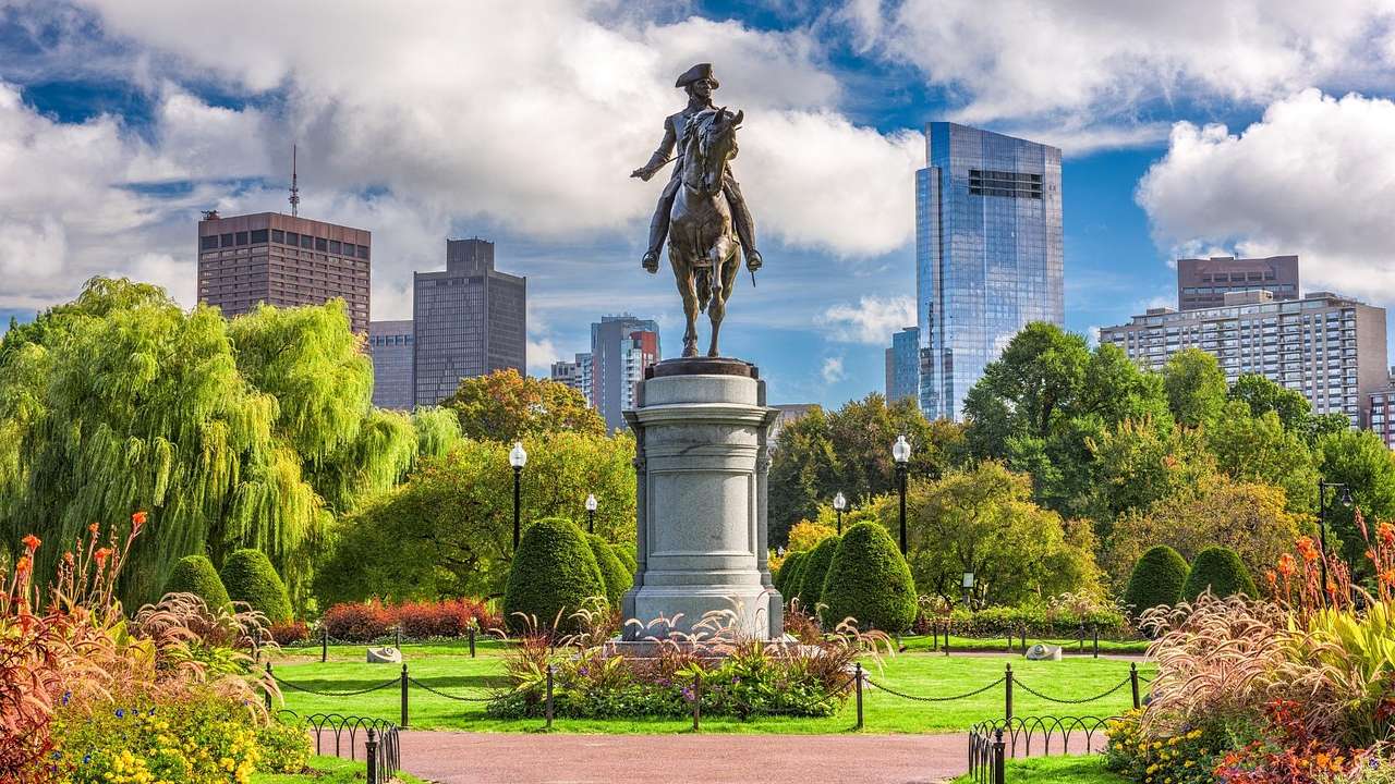 A statue in a park with grass and trees and a city skyline behind it