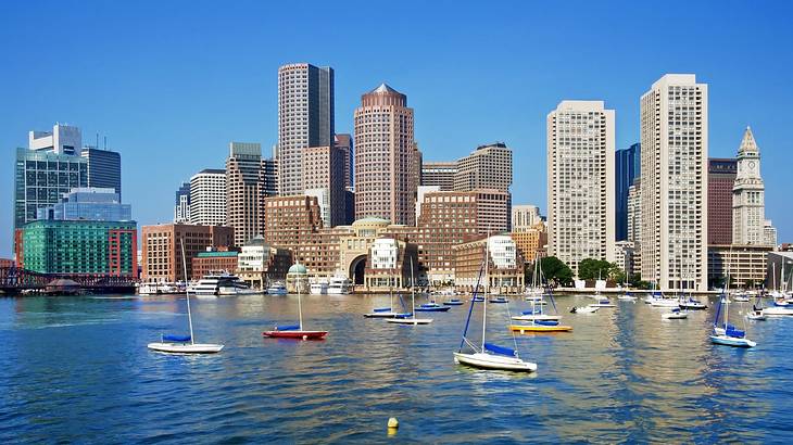 A city skyline with skyscrapers and a harbor in front of it with boats on it