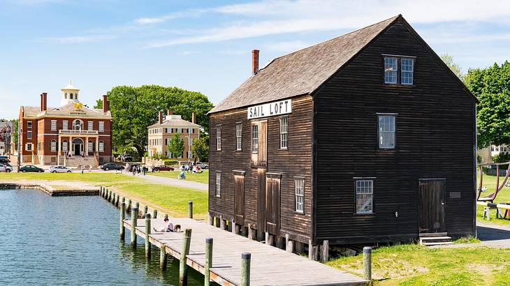 An old wooden barn structure next to a river with a mansion in the background