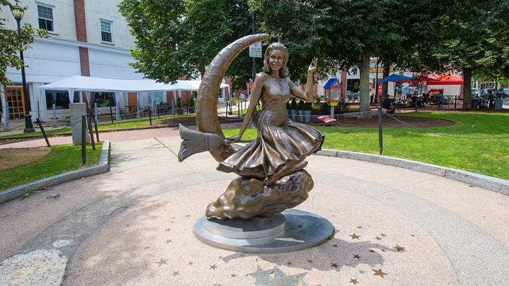 A bronze statue of a witch on a broomstick with a crescent moon behind her