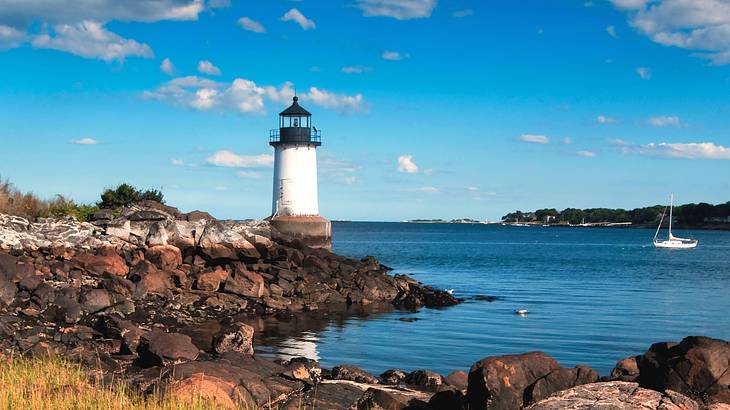 A white and black lighthouse surrounded by rocks with water beside it