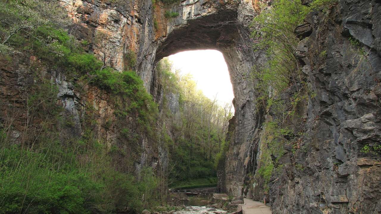 A natural stone arch with a river running through it and greenery surrounding it