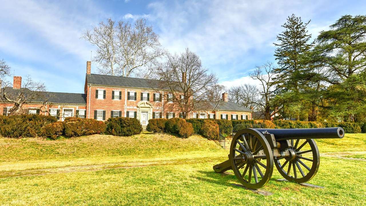 An old-fashioned redbrick house was grass and a cannon in front of it