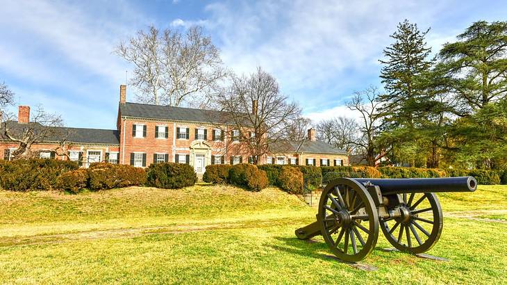 An old-fashioned redbrick house was grass and a cannon in front of it