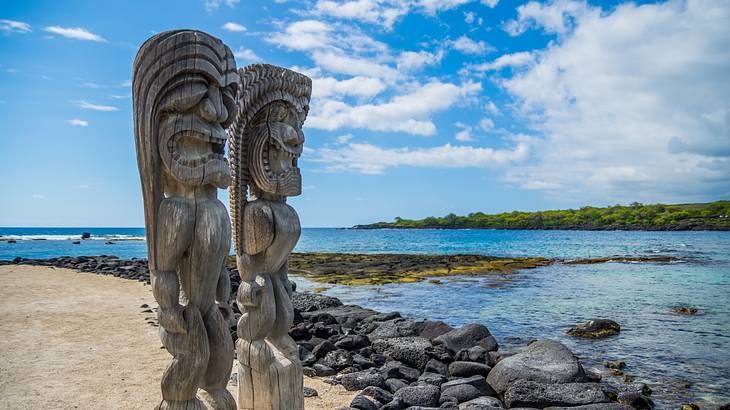 Tall wooden carvings on a rocky beach with a partly cloudy blue sky in the background Tall wooden carvings on a rocky beach with a partly cloudy blue sky in the background