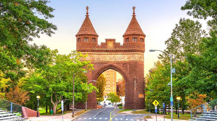 An archway with two towers and a road running through it surrounded by trees