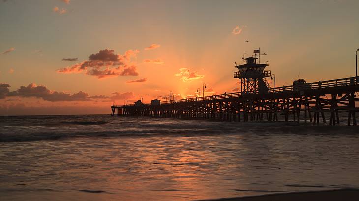 The sun setting over a pier that stretches out into the sea